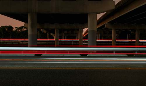 light trail timelapse photography of vehicle light crossing on road under concrete dock long exposure